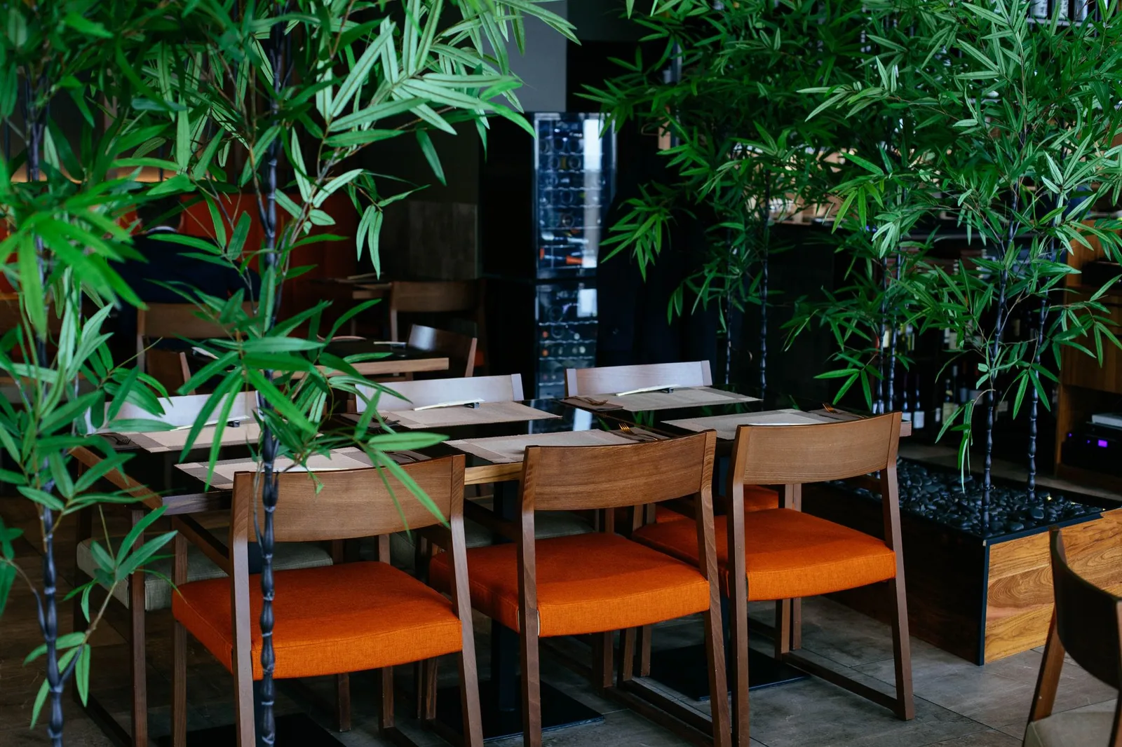Inviting restaurant interior with orange chairs and bamboo plants, offering a calm dining atmosphere.