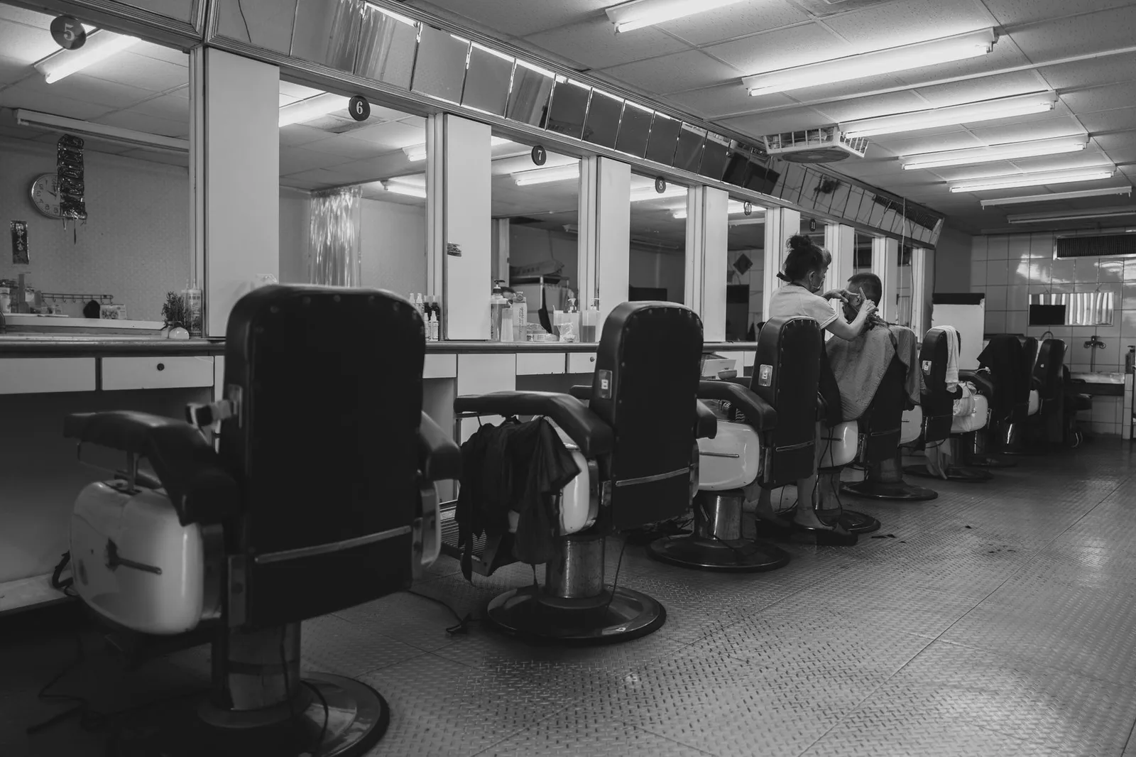 A black and white photo of a vintage barbershop with styling chairs and mirrors.
