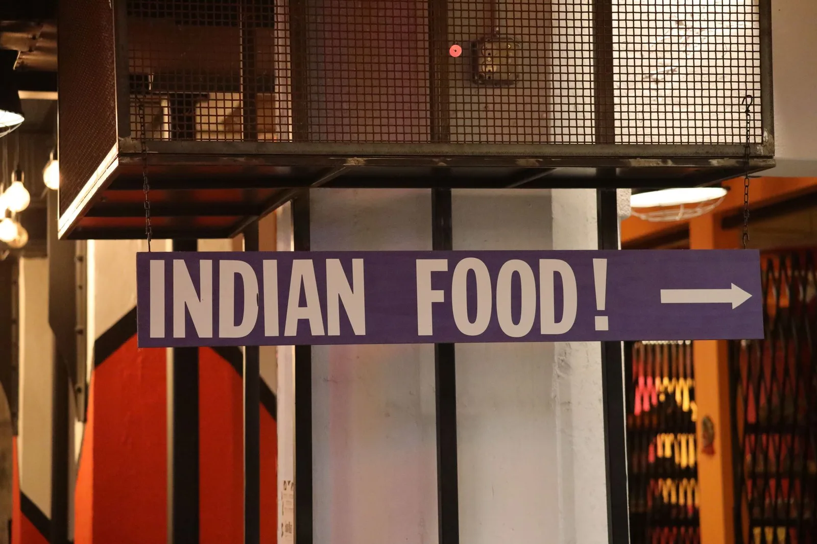 Indoor setting with a large sign reading 'Indian Food' pointing directionally.