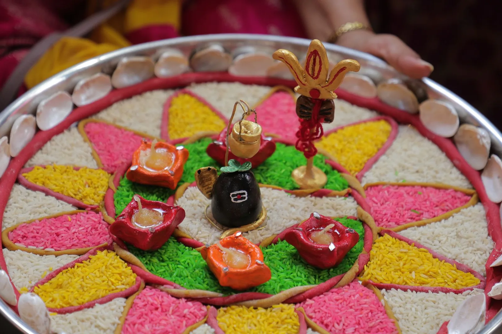 Vibrant decorative plate with rice, candles, and shells used in an Indian ceremony.