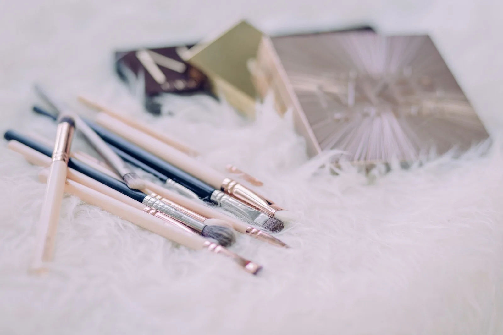 A chic arrangement of makeup brushes and palettes on a fluffy white surface, perfect for beauty and lifestyle themes.