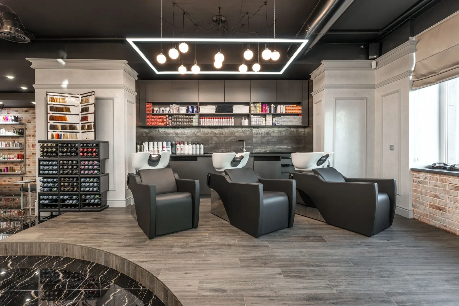 Black leather backwash chairs with sinks under glowing lamps placed in modern spacious beauty salon with cosmetology pro