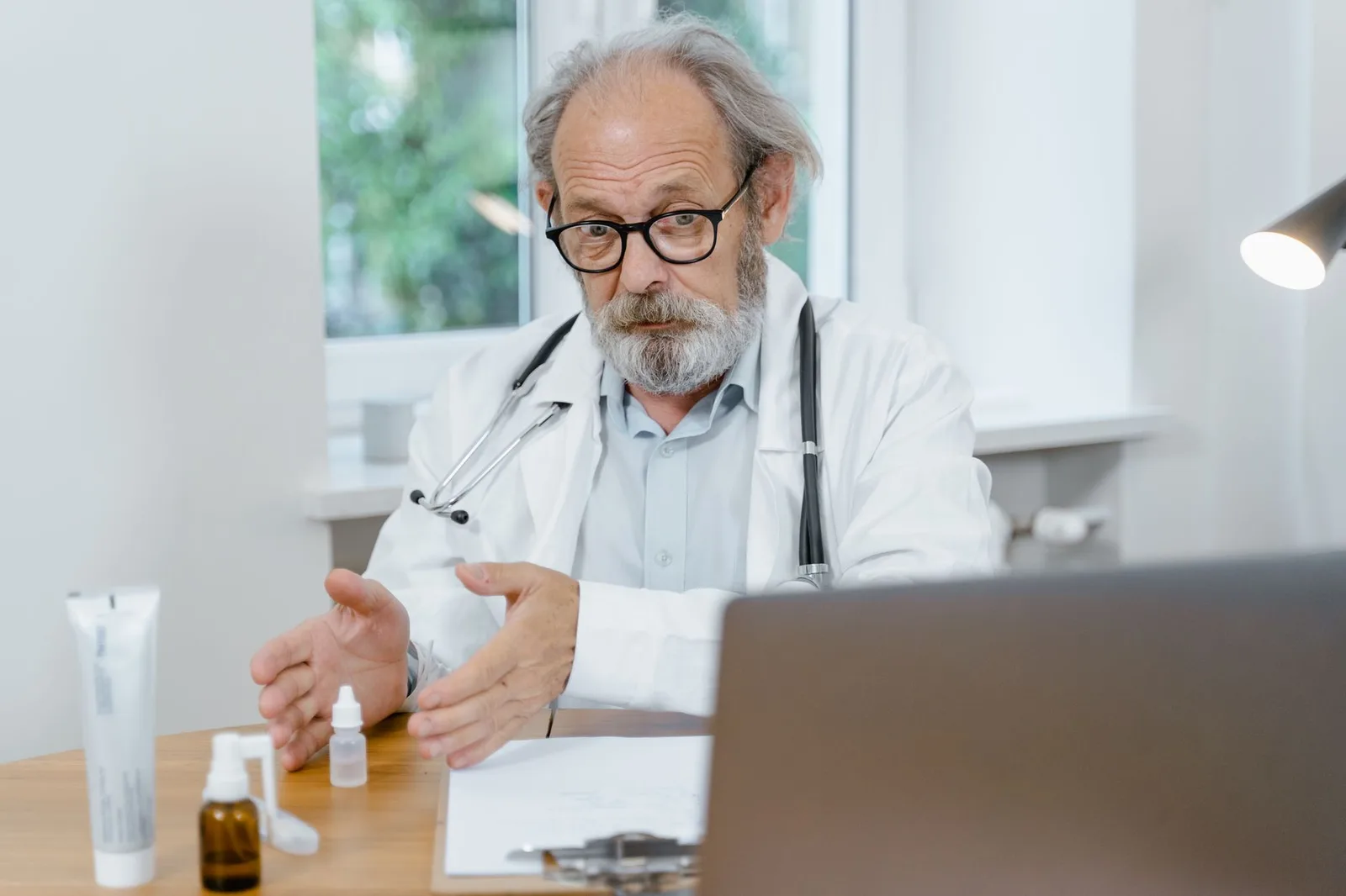 An elderly doctor in a white coat conducting an online medical consultation, focusing attentively.