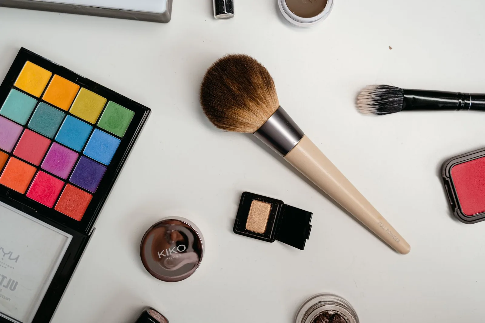 A vibrant flat lay of makeup essentials including a colorful palette and brushes on a white surface.