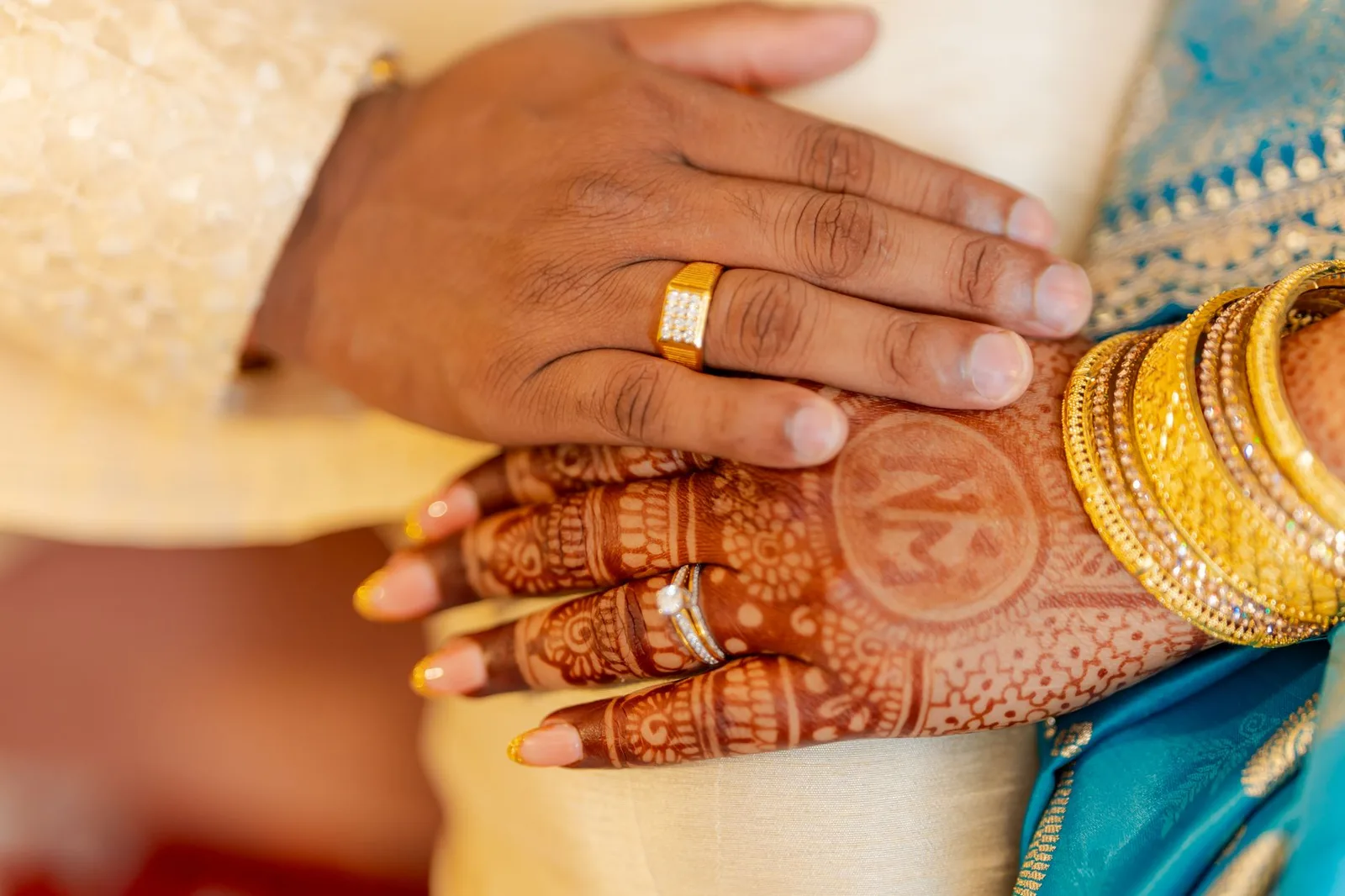 Close-up of South Asian bridal henna with gold jewelry and matching rings, showcasing cultural elegance.