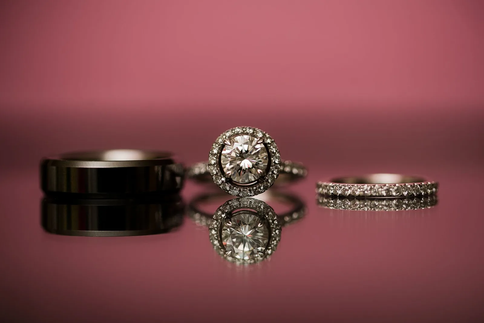 Close-up of wedding and engagement rings with diamonds on a reflective surface.